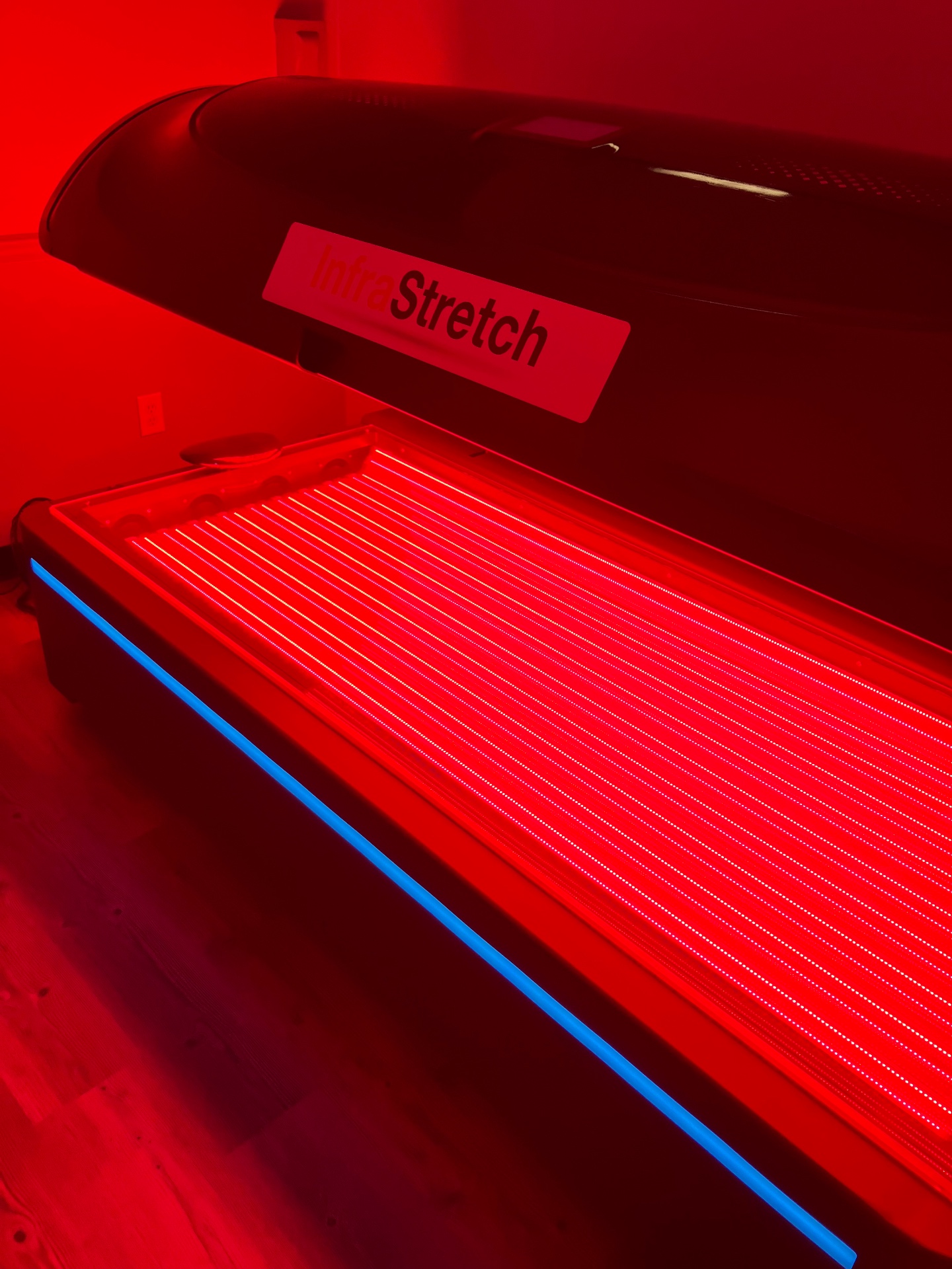The InfraStretch full-body red light and near-infrared bed with its canopy raised, showing the glowing light panels inside.