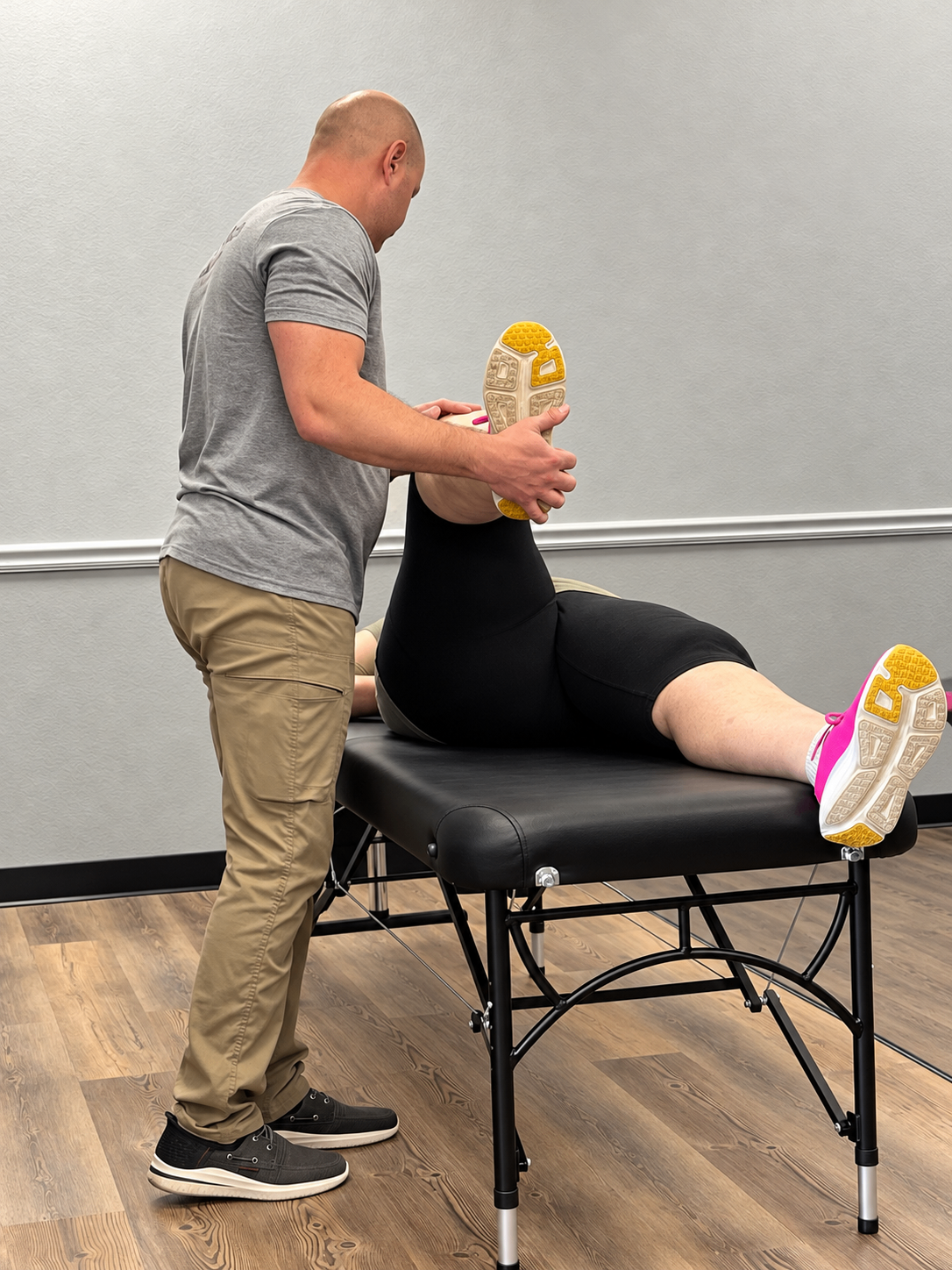 Jonathan guides a client through an assisted leg stretch while she lies on a treatment table.
